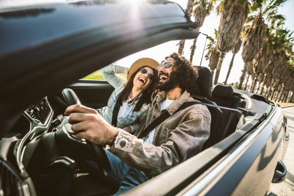 Happy couple driving convertible car enjoying summer vacation